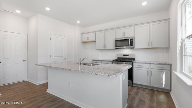 kitchen with a center island with sink, sink, appliances with stainless steel finishes, and dark wood-type flooring