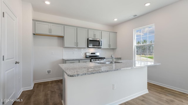 kitchen featuring light stone countertops, stainless steel appliances, a center island with sink, and gray cabinetry