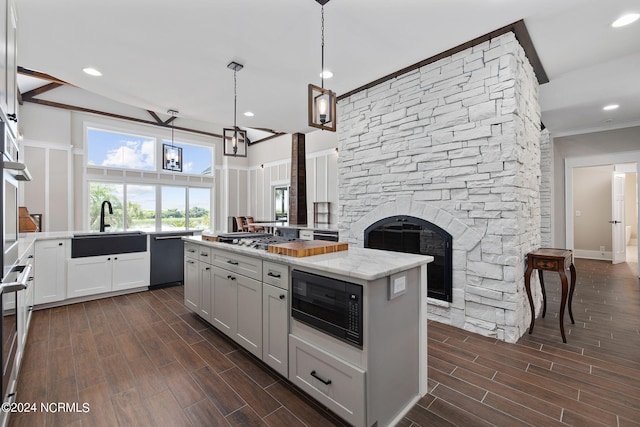 kitchen with stainless steel appliances, sink, pendant lighting, white cabinetry, and a stone fireplace