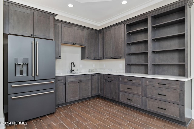 kitchen with high end fridge, sink, dark brown cabinetry, and crown molding