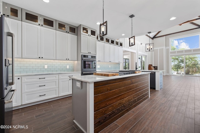 kitchen featuring light stone countertops, stainless steel appliances, decorative light fixtures, white cabinets, and a center island