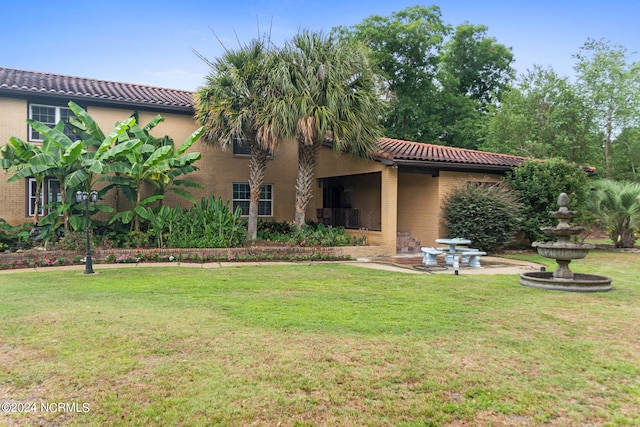 back of property featuring a yard, brick siding, a patio area, and a tile roof