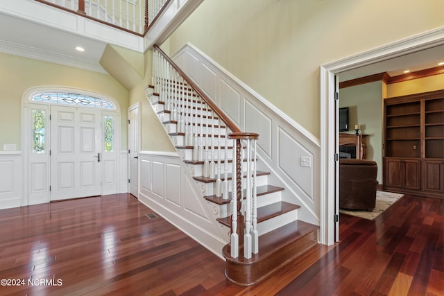 foyer with hardwood / wood-style flooring, a decorative wall, a wainscoted wall, a high ceiling, and ornamental molding