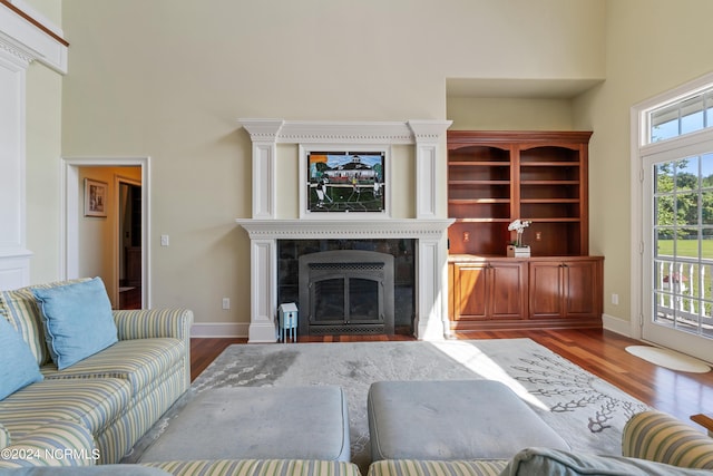 living area with a high end fireplace, a towering ceiling, baseboards, and wood finished floors