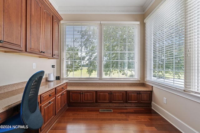 unfurnished office featuring baseboards, visible vents, built in study area, dark wood-style flooring, and crown molding