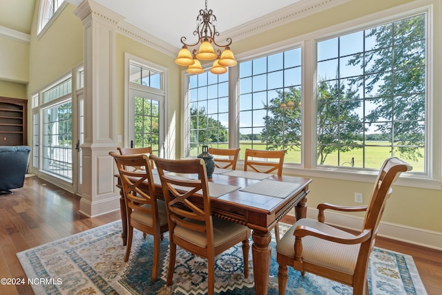 dining space with a notable chandelier, decorative columns, ornamental molding, wood finished floors, and baseboards