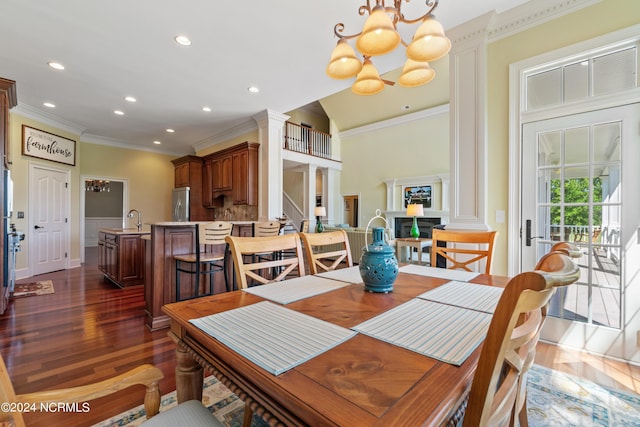 dining space with sink, dark hardwood / wood-style floors, decorative columns, a chandelier, and ornamental molding