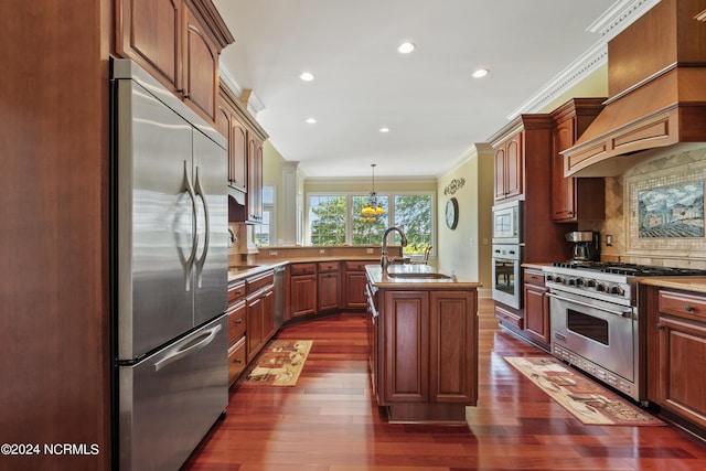 kitchen featuring sink, built in appliances, pendant lighting, a kitchen island with sink, and ornamental molding