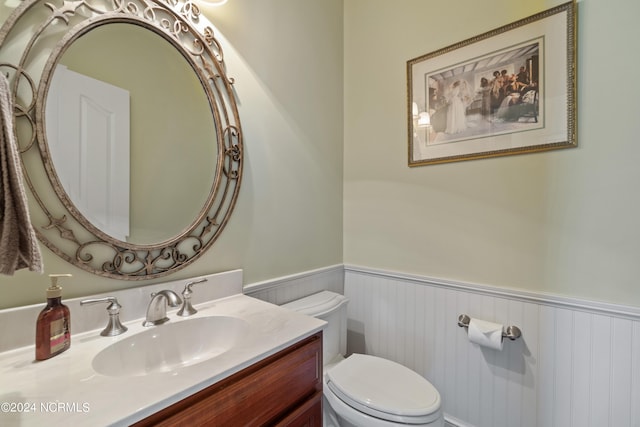 half bath with a wainscoted wall, vanity, and toilet