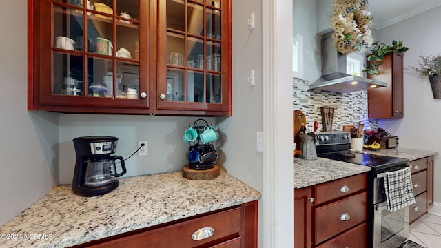 kitchen with crown molding, light stone counters, wall chimney range hood, range with two ovens, and backsplash