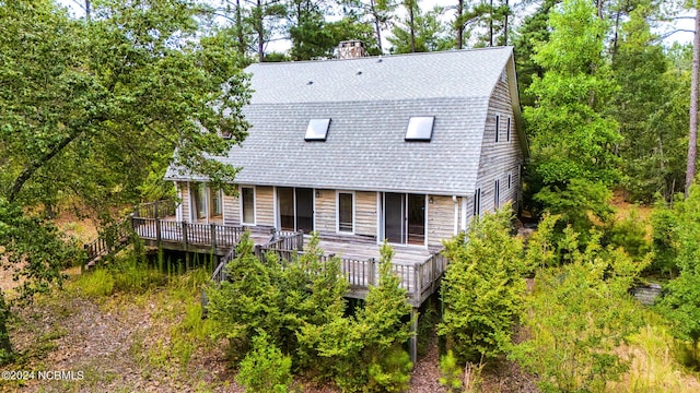 rear view of property featuring roof with shingles, a wooden deck, and a chimney