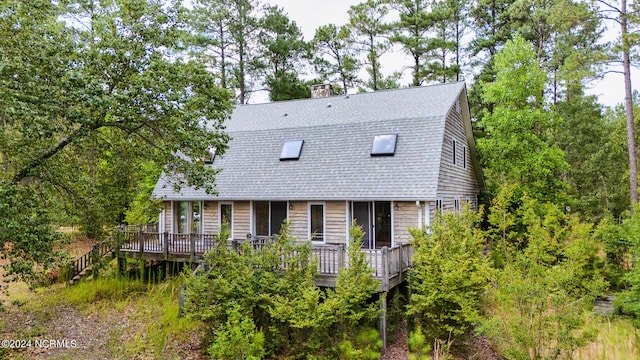back of house with roof with shingles, a wooden deck, and a chimney