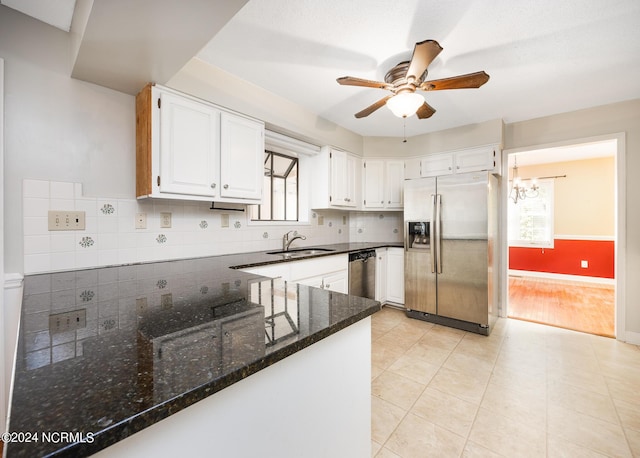 kitchen with appliances with stainless steel finishes, a sink, ceiling fan with notable chandelier, dark stone countertops, and decorative backsplash