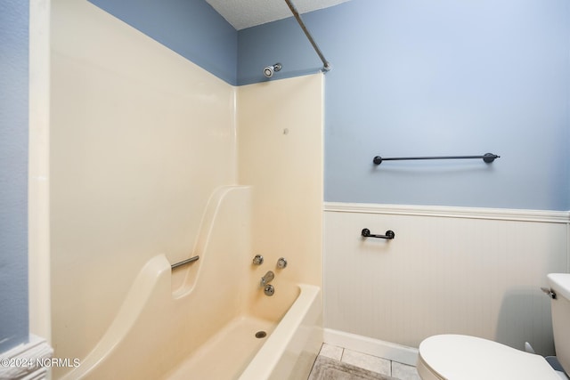 bathroom with toilet, baseboards, shower / tub combination, tile patterned floors, and a wainscoted wall
