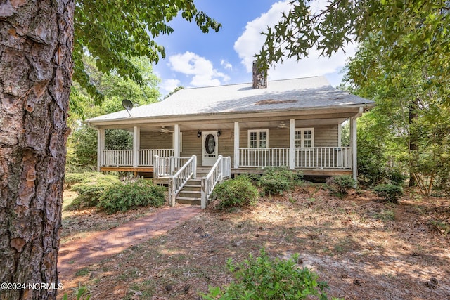 view of front of property featuring ceiling fan, roof with shingles, covered porch, and a chimney