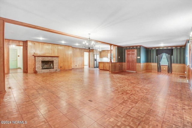 unfurnished living room with a brick fireplace, an inviting chandelier, and wood walls