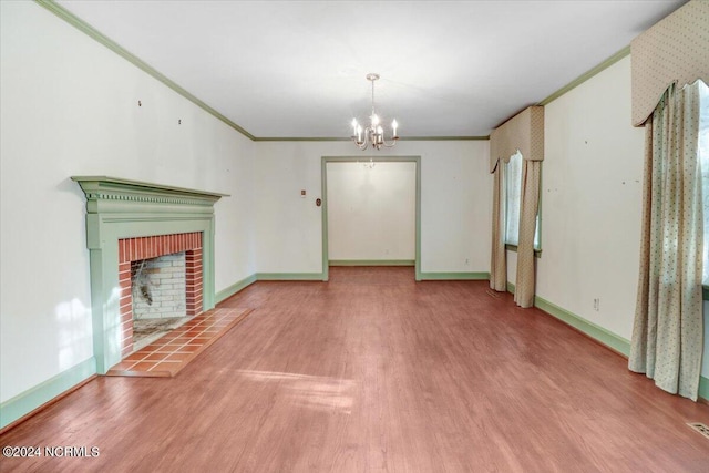 unfurnished living room with a brick fireplace, hardwood / wood-style flooring, ornamental molding, and a chandelier