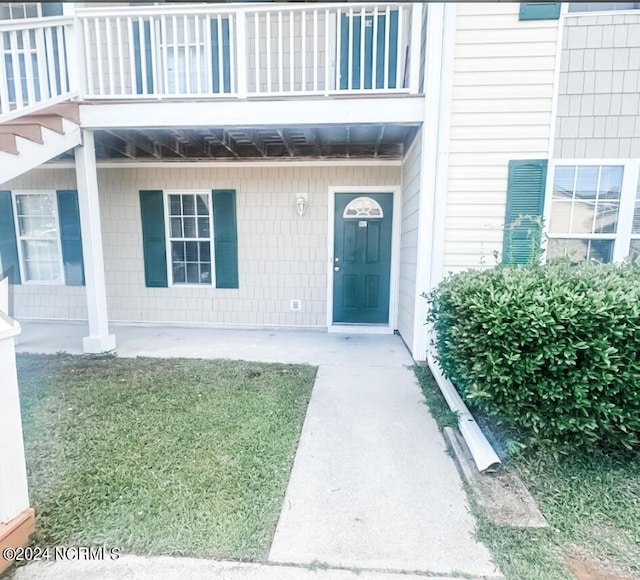 view of exterior entry with a balcony and a yard