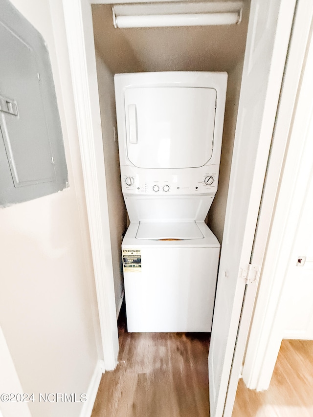 laundry room featuring electric panel, light wood-type flooring, and stacked washing maching and dryer