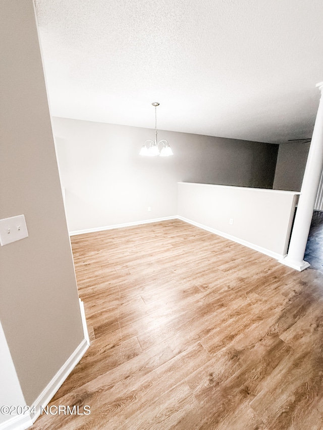 unfurnished room featuring a notable chandelier, a textured ceiling, and wood-type flooring