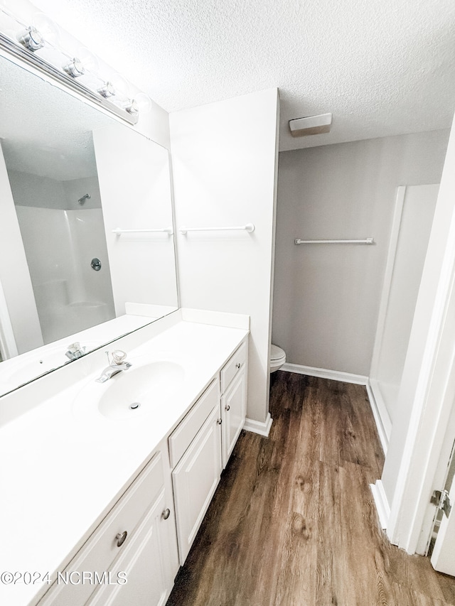 bathroom featuring hardwood / wood-style floors, a textured ceiling, a shower, toilet, and vanity