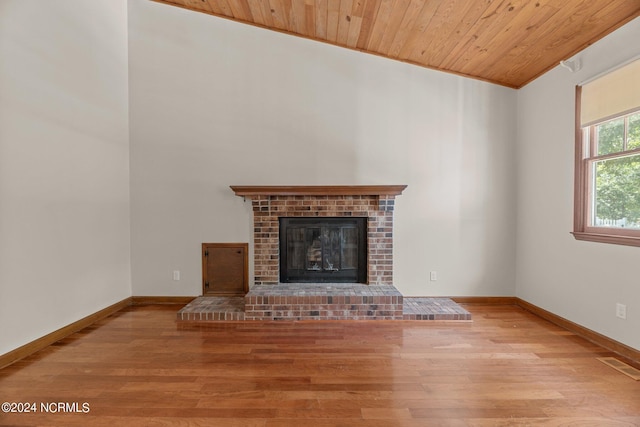 unfurnished living room featuring wooden ceiling, baseboards, a brick fireplace, and wood finished floors