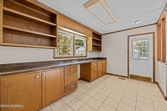 kitchen with crown molding, a healthy amount of sunlight, built in desk, and light tile patterned floors