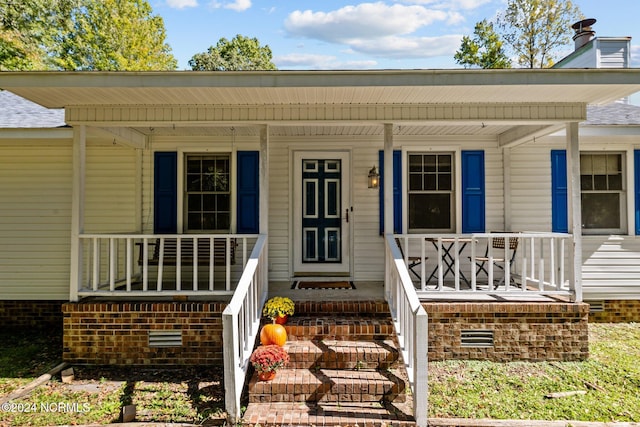 view of exterior entry with a chimney and a porch