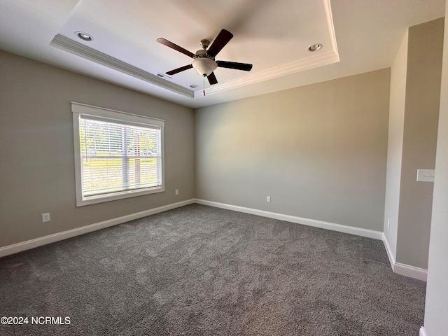 unfurnished room with a ceiling fan, a tray ceiling, dark carpet, and baseboards