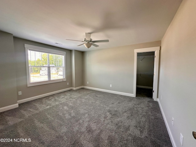 empty room featuring dark colored carpet, a ceiling fan, visible vents, and baseboards