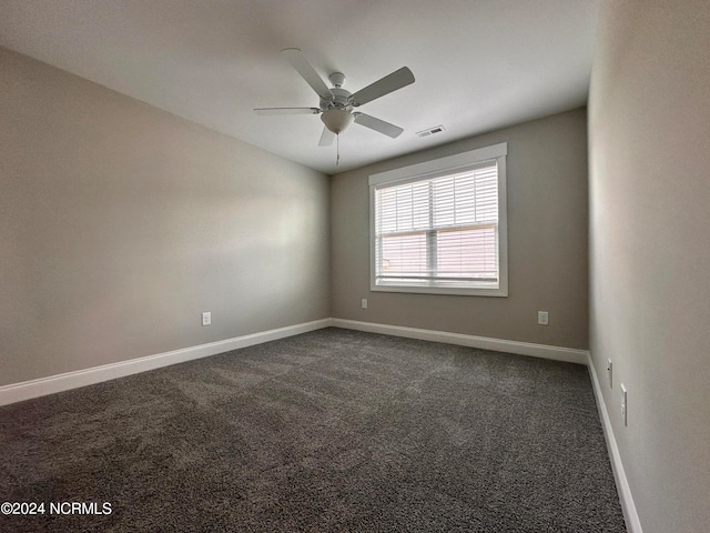 spare room with a ceiling fan, dark colored carpet, visible vents, and baseboards