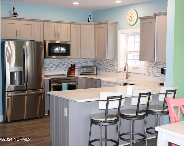 kitchen with dark wood-type flooring, kitchen peninsula, backsplash, and stainless steel appliances