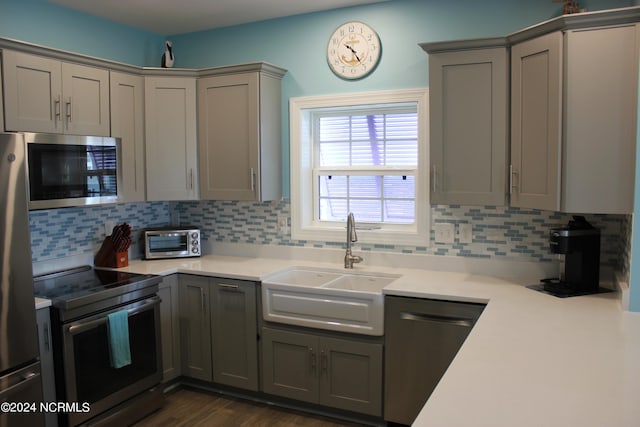 kitchen with gray cabinets, stainless steel appliances, dark hardwood / wood-style flooring, and tasteful backsplash