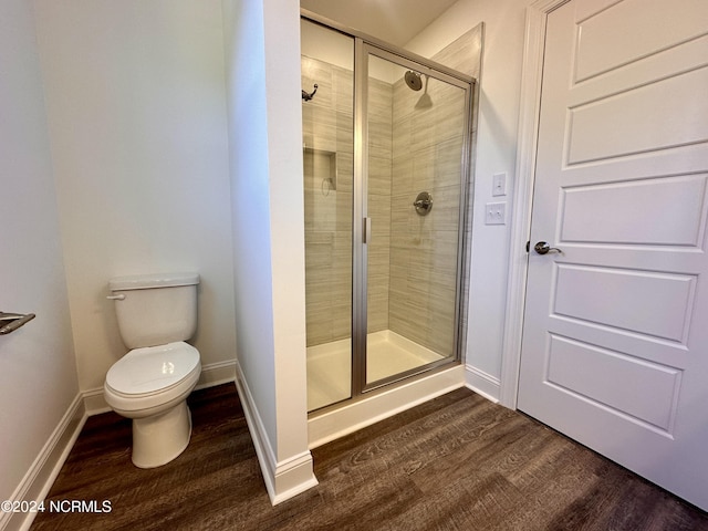 bathroom with toilet, a stall shower, baseboards, and wood finished floors