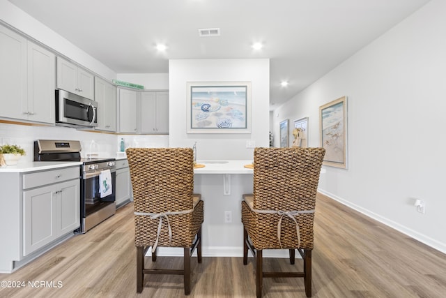 kitchen with a kitchen bar, stainless steel appliances, light countertops, and gray cabinetry