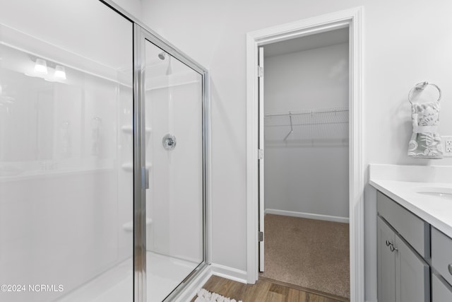 bathroom with wood finished floors, vanity, baseboards, a spacious closet, and a shower stall