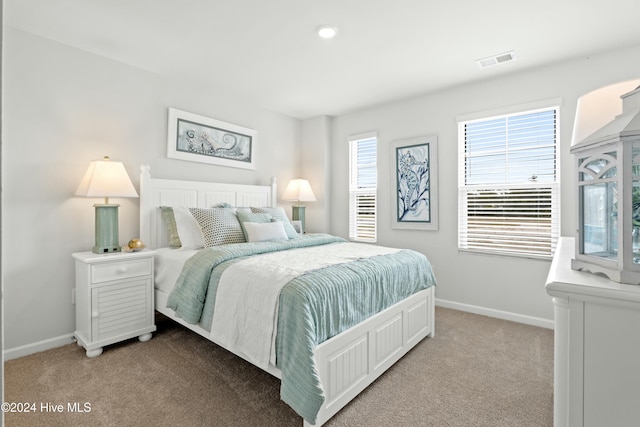 bedroom featuring baseboards, multiple windows, visible vents, and light colored carpet