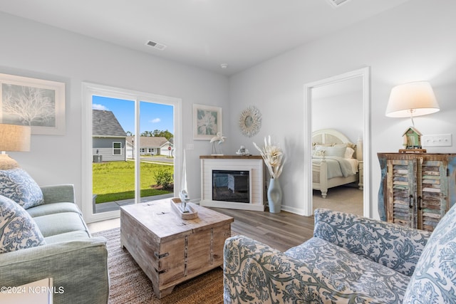 living area featuring wood finished floors, a glass covered fireplace, visible vents, and baseboards