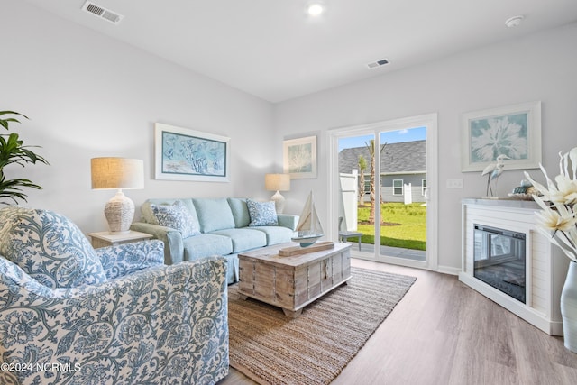 living room featuring a glass covered fireplace, visible vents, and wood finished floors