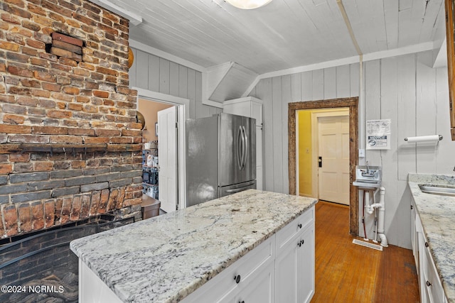 kitchen featuring dark hardwood / wood-style flooring, wooden walls, white cabinetry, light stone countertops, and stainless steel fridge