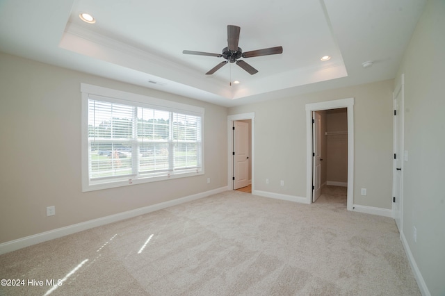 unfurnished bedroom featuring ceiling fan, a closet, a walk in closet, and a tray ceiling