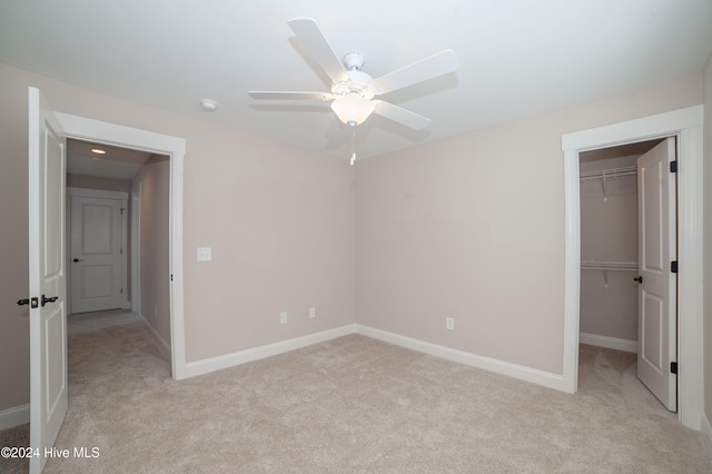 unfurnished bedroom featuring light carpet, ceiling fan, a walk in closet, and a closet