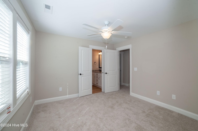 unfurnished bedroom featuring ceiling fan, ensuite bath, and light carpet