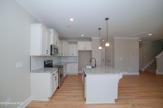 kitchen featuring white cabinets, stainless steel appliances, a center island with sink, and light stone countertops