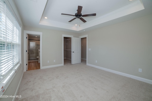 unfurnished bedroom with a spacious closet, ceiling fan, ensuite bath, and a tray ceiling