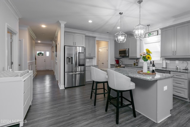 kitchen featuring appliances with stainless steel finishes, decorative light fixtures, gray cabinetry, a kitchen bar, and a center island