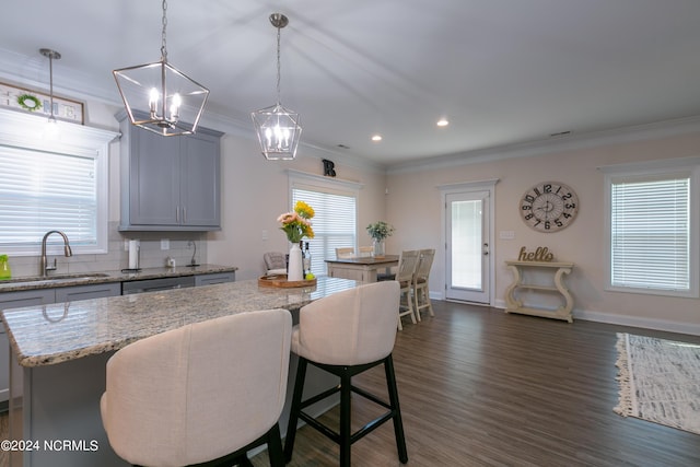 kitchen featuring a kitchen island, sink, hanging light fixtures, light stone counters, and crown molding