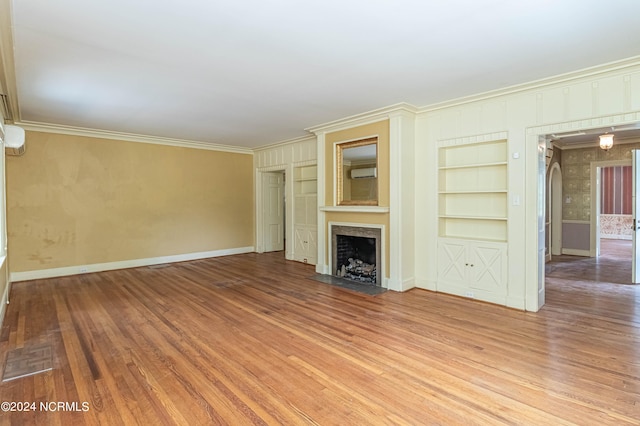 unfurnished living room featuring ornamental molding, light hardwood / wood-style flooring, a wall mounted air conditioner, and built in shelves