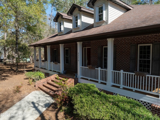 view of property exterior featuring brick siding, covered porch, and roof with shingles