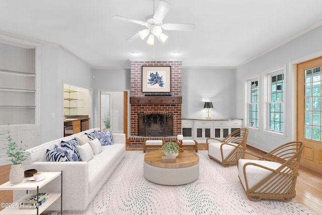 living room with a brick fireplace, baseboards, ornamental molding, wood finished floors, and a ceiling fan